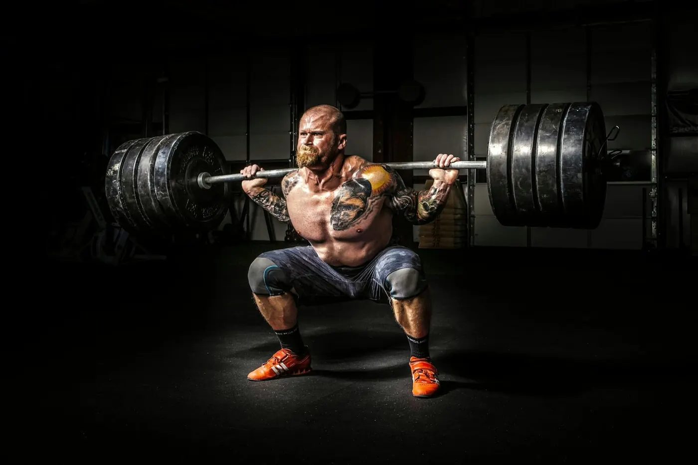 Powerlifter squatting a heavy barbell in a dark gym