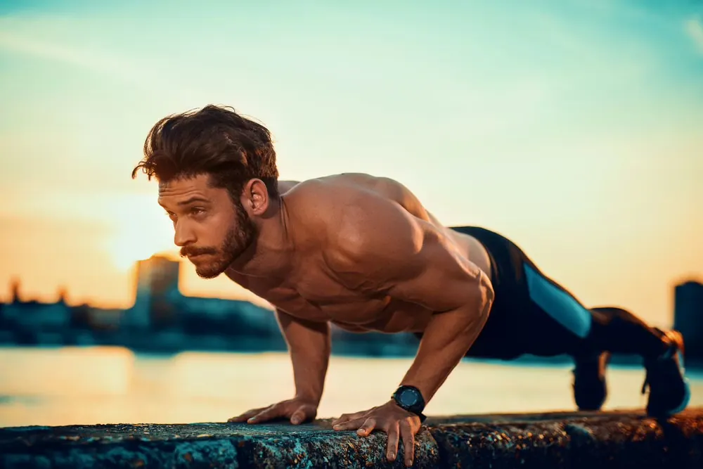Man doing a push-up on a waterfront wall at sunset