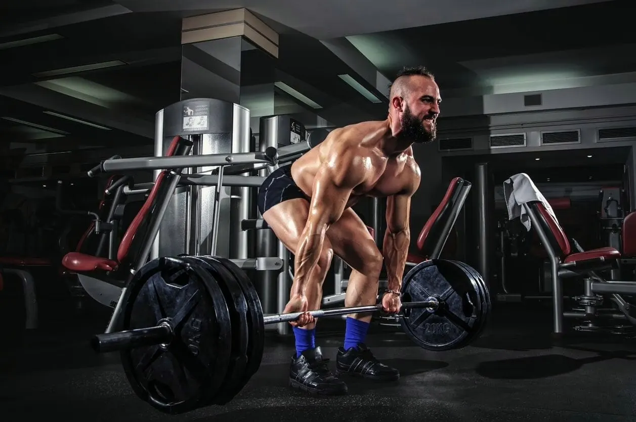 Man deadlifting a loaded barbell in a dark gym